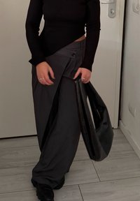 Haut noir à manches longues côtelé associé à un pantalon large gris avec bouton à l'avant et plis latéraux. Tient un sac cabas noir.
