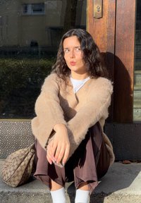 Lichtbeige, pluizige gebreide trui met brede mouwen, gecombineerd met donkerbruine wijde broekspijpen en witte sokken. Ernaast ligt een geborduurde bruine tas.