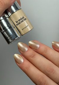 Gold and silver gel polish bottles with metallic caps; a hand with shimmering gold almond-shaped nails in focus. Smooth texture, glossy finish.
