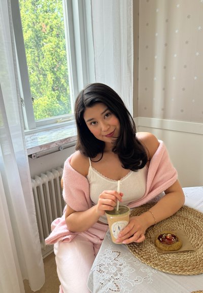 Suéter rosa suave colocado sobre una camiseta blanca, sosteniendo un batido en un vaso transparente, con una galleta sobre un tapete redondo de mimbre en un mantel estampado.