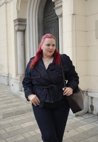 Veste en jean foncé avec une taille ceinturée ; assortie à un jean coordonné. Accessoirisée avec un sac à main foncé et des colliers superposés. Cheveux roses.