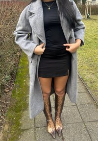 Um longo casaco de lã cinza sobre um vestido preto ajustado, combinado com botas de joelho em estampado de Onça castanho, com bicos pontiagudos.
