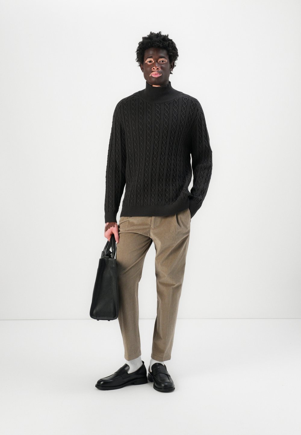 Črna pletena pulover s turtleneck ovratnikom in teksturiranim vzorcem, bež prugaste hlače, črna usnjena torba in črne slip-on čevlje z belimi nogavicami.