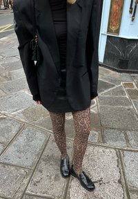 Zwarte oversized blazer over een zwarte top, gecombineerd met bruin leopardenprint panty's en zwarte instappers. Achtergrond van stenen straat.