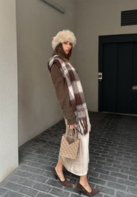 Brown wool jumper, plaid scarf featuring white and brown tones, beige satin skirt, brown suede heels, and a textured beige handbag.