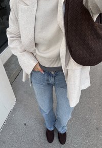 Világos bézs texturált blézer krémszínű kötött pulóverrel, világoskék, bővülő szárú farmerrel és sötétbarna szövött táskával párosítva.