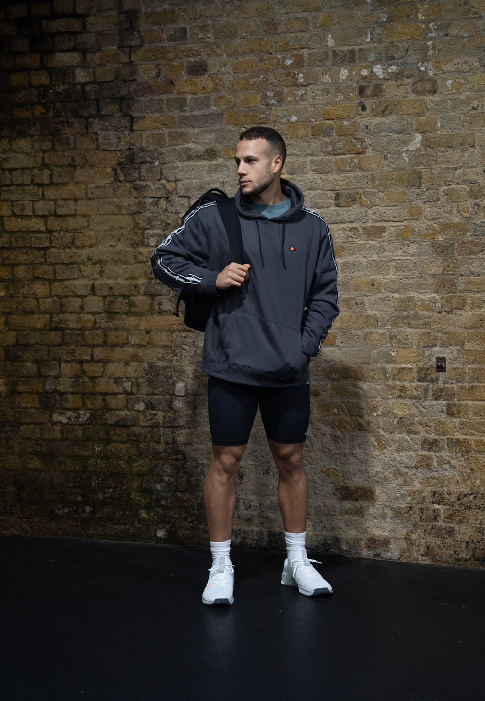 Γκρίζα φούτερ με καγκουρό τσέπη, λευκές πλευρικές ρίγες, συνδυασμένο με μαύρες βερμούδες. Λευκά αθλητικά παπούτσια και μια μαύρη τσάντα πλάτης ολοκληρώνουν την εμφάνιση.