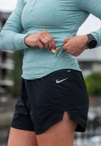 Długi rękaw, jasnoniebieska bluzka z połową zamka błyskawicznego, w połączeniu z czarnymi szortami z boczną kieszenią i logo Nike na lewym dolnym rogu.