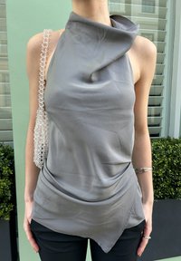 Haut gris sans manches avec un col drapé et un ourlet asymétrique. Comprend un sac à main transparent embelli de perles sur l'épaule gauche. Texture lisse.