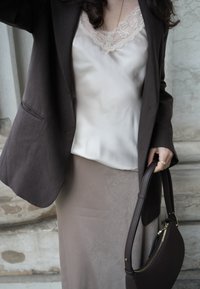 Rjav blazer preko kremaste svilenkaste bluze z čipkasto obrobo in dolge bež krila. Obleko dopolnjuje teksturirana rjava torbica.