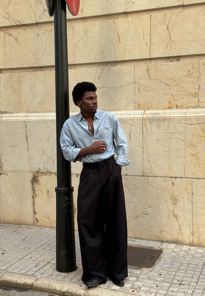 Camisa azul claro abotonada con un detalle bordado, combinada con pantalones anchos negros. La textura es suave y el ajuste es cómodo.