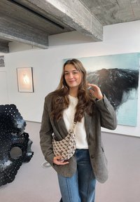 Beige patterned shoulder bag with a gold chain strap, crafted from soft fabric. Grey blazer worn over a white top, styled with wide-leg jeans.