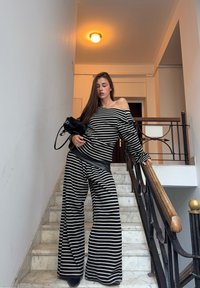 Tenue rayée noire et blanche comprenant un haut à épaules dénudées et un pantalon pattes d'éléphant. Accessoires : un petit sac à main. Scène située sur un escalier.