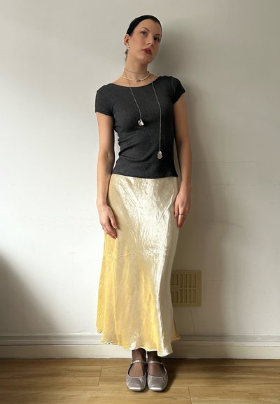 Top negro de manga corta acanalado, falda de satén crema y amarilla, zapatos de tacón bajo plateados, collares de plata en capas, textura suave, corte simple.