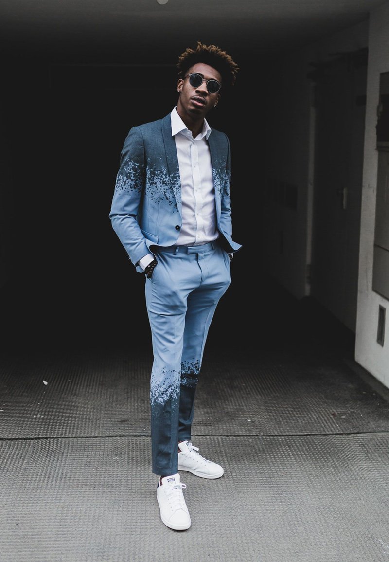 Light blue suit with a gradient splatter design, paired with a white shirt and white sneakers. The suit features a smooth texture and a tailored fit, complemented by round sunglasses as an accessory.