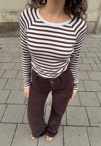 Top de manga larga a rayas marrón y blanca combinado con pantalones acampanados de pana marrón. El conjunto presenta un escote redondeado y tela texturizada.