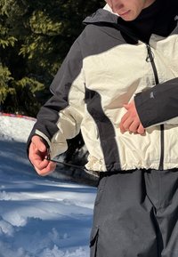 Bundová bunda s černobílým barevným blokováním, zkrácený střih, staženým pasem, nastavitelnou šňůrkou, předním zipem a kapsami.