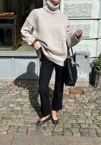 Beige oversized polotröja, svarta flarebyxor, svart axelväska, prickiga ballerinas. Texturerad stickning och kontrasterande färger.