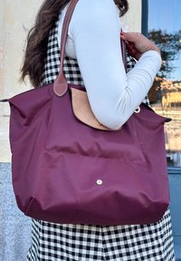 Bolsa tote bordeaux com um bolso de tecido bege, textura suave e alças de couro castanho. Apresenta um fecho com botão de pressão e um design casual.