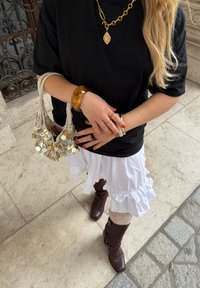 Fekete, oversize póló, fehér, fodros szoknya, barna bőr, térd fölé érő csizma, sárga karkötő, arany nyaklánc, és egy textúrált kézitáska aprópénzzel.
