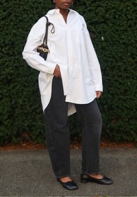 Biała, luźna koszula na guziki z długimi rękawami, zestawiona z czarnymi, wysokim stanem dżinsami i czarnymi balerinami. Czarna torebka na łańcuszku.