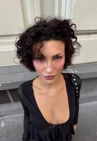 Top nero con scollatura a V profonda e dettaglio con cravatta. Presenta maniche trasparenti e una vestibilità rilassata. Accentato da una borsa nera con borchie.