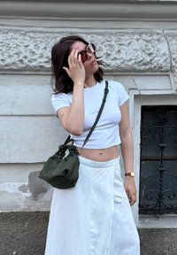 Λευκό cropped tshirt, πράσινη τσάντα με φιόγκους, και λευκή φούστα wrap. Καφέ ρολόι στον καρπό, και oversized γυαλιά ηλίου με καφέ φακούς.