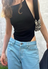 Bodies preto canelado com design de um ombro, combinado com jeans de ganga azul claro com um layout clássico de cinco bolsos e fecho de botão.