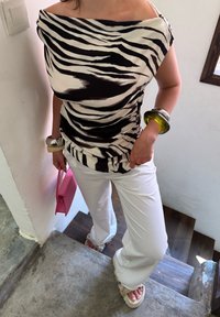 Zwart-wit gestreepte off-shoulder top, witte broek en oversized armbanden. Houdt een roze handtas vast; staat op een trap.