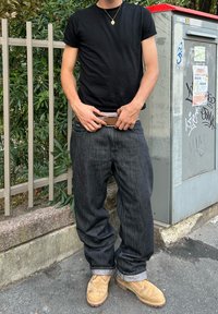 Black short-sleeved t-shirt, loose-fitting dark denim jeans, brown belt, and tan work boots, featuring rolled cuffs and a rugged texture.