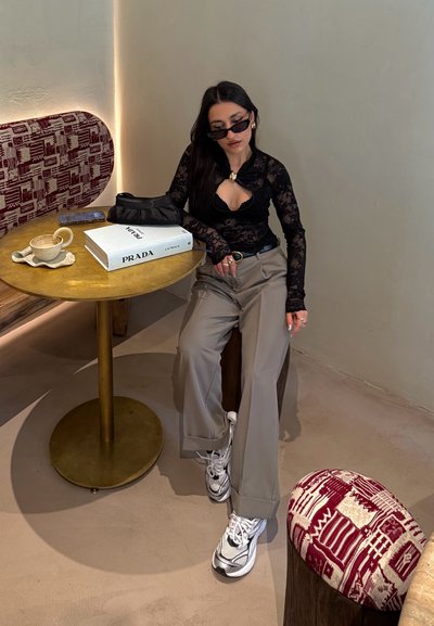 Top negro de encaje de manga larga, pantalones sueltos beige, zapatillas plateadas gruesas, mesa redonda dorada, tapicería con estampado, caja de Prada, taza de café.