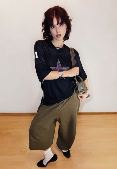 Jersey negro de gran tamaño con un diseño de estrella brillante, combinado con pantalones anchos de color verde oliva. Los accesorios incluyen una pulsera plateada y un bolso pequeño.