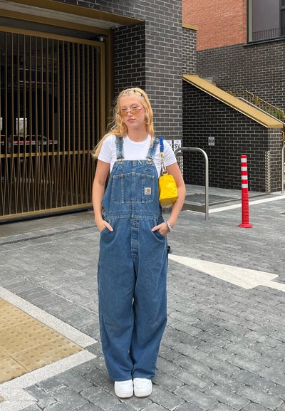 Pantalones de mezclilla con corte relajado, lavado azul, bolsillos frontales, llevados sobre una camiseta blanca. Acentuados con un bolso amarillo y zapatillas blancas.