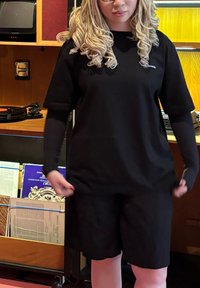 Melna lielā izmēra t-kreklis un atbilstošas šortus, izgatavoti no gludas auduma, ar īsām piedurknēm un brīvu piegriezumu. Iekļauj minimālu zīmola noformējumu.