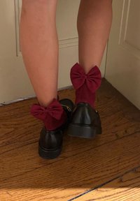 Μαύρα παπ�ούτσια με χοντρές σόλες, συνδυασμένα με μπορντό κάλτσες μέχρι τον αστράγαλο που έχουν μεγάλες λεπτομέρειες με φιόγκο στην κορυφή. Φόντο ξύλινο δάπεδο.