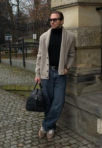 Cardigan gris clair côtelé porté sur un col roulé noir, associé à un jean bleu foncé et des baskets beige. Tenant un sac en cuir noir.