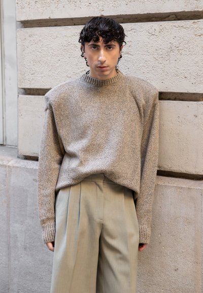 Suéter de punto beige con textura y cuello alto, combinado con pantalones plisados gris claro, creando una silueta relajada.