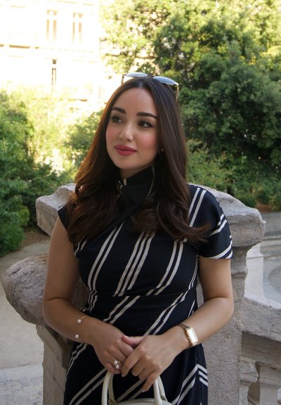 Vestido negro con rayas verticales blancas, mangas cortas y un cuello alto. Los accesorios incluyen una pulsera, un anillo y un bolso blanco.