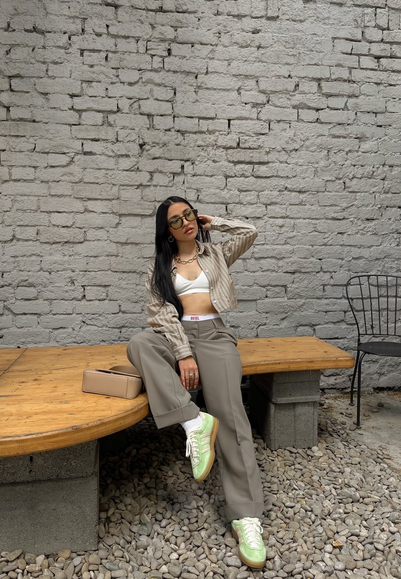 Ριγέ μπεζ και λευκό κοντό πουκάμισο πάνω από ένα λευκό tank top, συνδυασμένο με μπεζ παντελόνι σε φαρδιά γραμμή και πράσινα αθλητικά παπούτσια. Μινιμαλιστική μπεζ τσάντα.