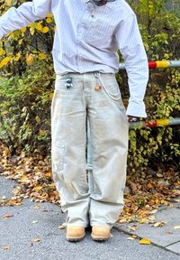 Gaiši bēšas brīvā stila bikses ar kabatām cargo stilā, izgatavotas no faktūras auduma, papildinātas ar ķēdēm un piekariņiem. Valkātas kopā ar brūnām zābakām un svītrainu kreklu.