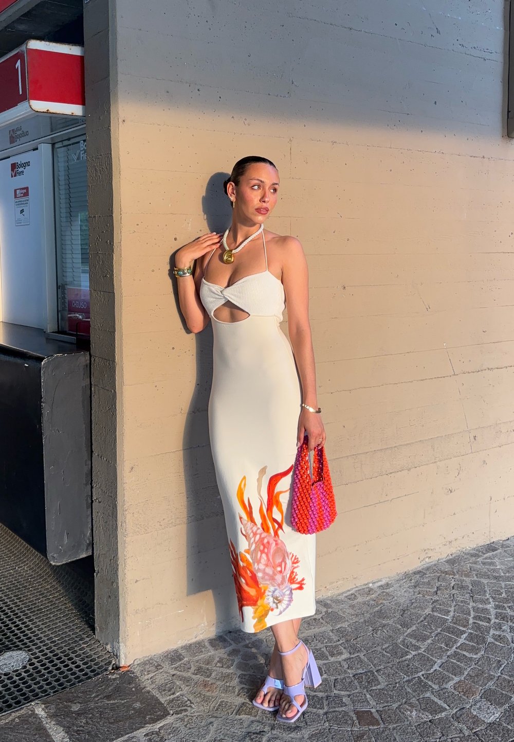 Vestido midi blanco con un detalle recortado y un estampado floral colorido. Combinado con tacones lavanda y un bolso texturizado rosa.