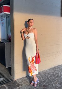 Vestido midi blanco con un detalle recortado y un estampado floral colorido. Combinado con tacones lavanda y un bolso texturizado rosa.