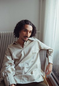 Lichtbeige oversized shirt met een brede kraag en lange, geraffineerde mouwen. Soepele stof met knoopaccenten. Informele binnenomgeving.