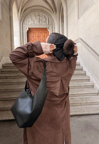 Rudas zomšinis paltas su skeltuku gale, juoda rankinė, rankogaliai su nėriniais ir didelė juoda plaukų juosta. Fone - akmeninės laiptinės.