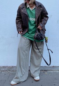 Καφέ δερμάτινο μπουφάν πάνω από ένα πράσινο μπλούζα της Adidas, μπεζ παντελόνι σε φαρδιά γραμμή, άσπρα παπούτσια με καφέ σόλες και μία μικρή μαύρη τσάντα.