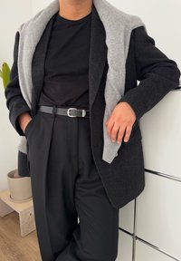 Μαύρο βαμβακερό σακάκι με γκρίζο πουλόβερ ριγμένο στους ώμους. Μαύρη μπλούζα, ψηλόμεσες μαύρες παντελόνες και δερμάτινη ζώνη. Σύγχρονη, κομψή γραμμή.