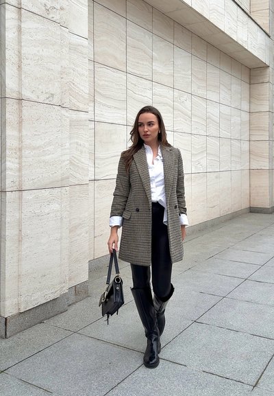 Blazer de patrón de espiga con un corte ajustado, combinado con una camisa blanca y pantalones de cuero negros, accessorios con un bolso pequeño y botas hasta la rodilla.