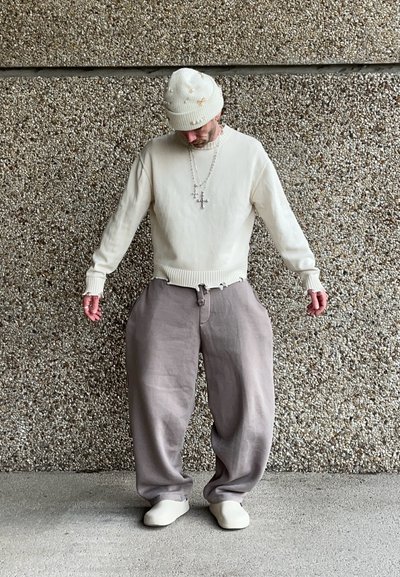 Suéter crema con puños acanalados, pantalones grises holgados y zapatillas blancas sin cordones. Acentuado con un gorro de color claro y collares en capas.