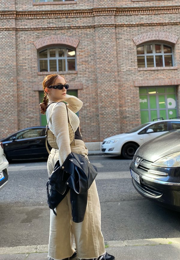 Suéter de punto en color crema, pantalones de tiro alto beige de pierna ancha y chaqueta de cuero negra. Los accesorios incluyen gafas de sol y un bolso negro.