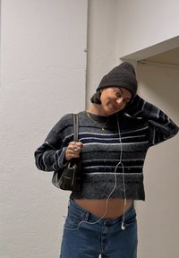 Pull à rayures épaisses gris avec des lignes bleues et blanches, associé  à un jean bleu taille haute. Accessoires : un sac à main noir et des écouteurs.